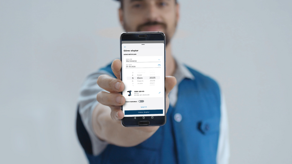 Seorang pria menunjukkan smartphone dengan aplikasi yang menampilkan rincian tugas. Dia mengenakan kemeja biru.