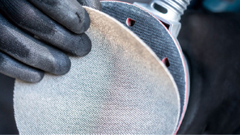 Dua tangan dengan sarung tangan hitam memegang cakram penggiling.