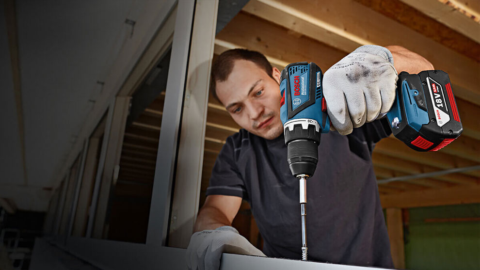 Seorang pria dengan bor nirkabel Bosch Professional memasang profil logam.