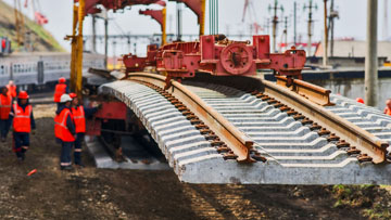 Pekerja berpakaian oranye sedang memasang rel dengan crane.