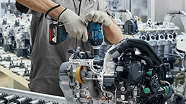 Seorang pekerja yang mengenakan helm dan masker pelindung menggunakan bor di perancah.