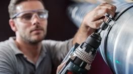 Seorang pengrajin dengan kacamata pelindung menggunakan bor hitam Bosch.