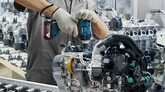 Seorang pekerja yang mengenakan helm dan masker menggunakan alat Bosch Professional.