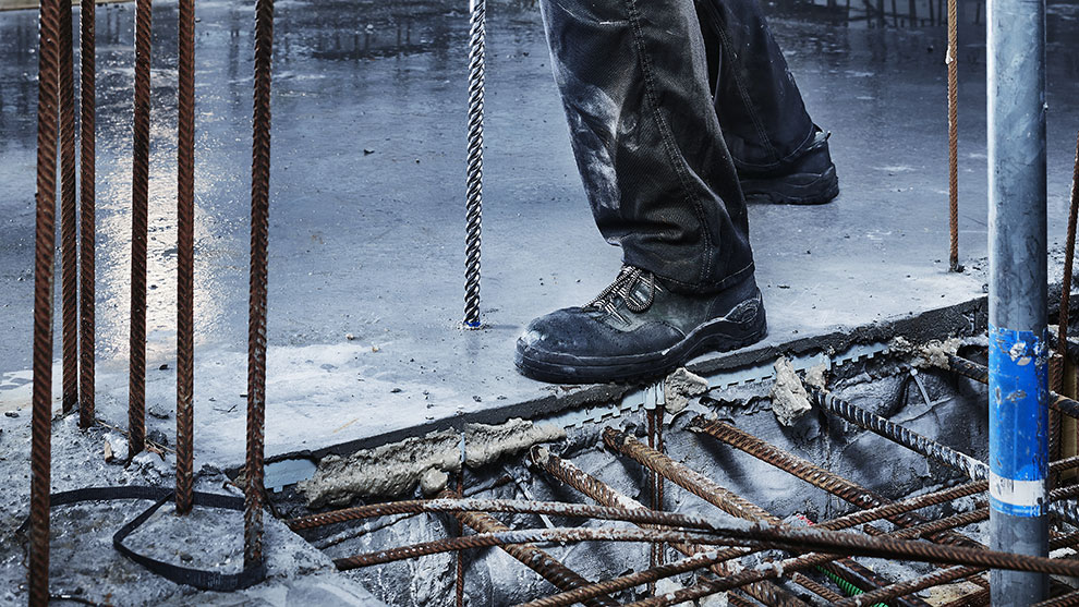 Seorang pekerja dengan sepatu bot hitam berdiri di atas permukaan beton.