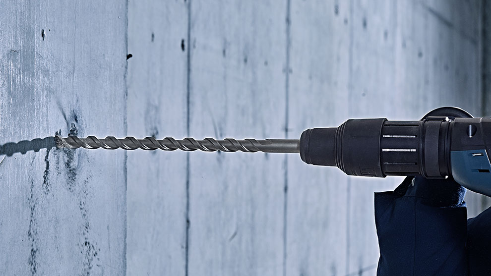 Sebuah bor Profesional Bosch dimasukkan ke dalam dinding beton.