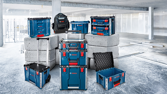 Beberapa kotak alat Bosch Professional berwarna biru dan hitam disusun di atas balok bangunan abu-abu. Sebuah ransel terletak di atasnya.