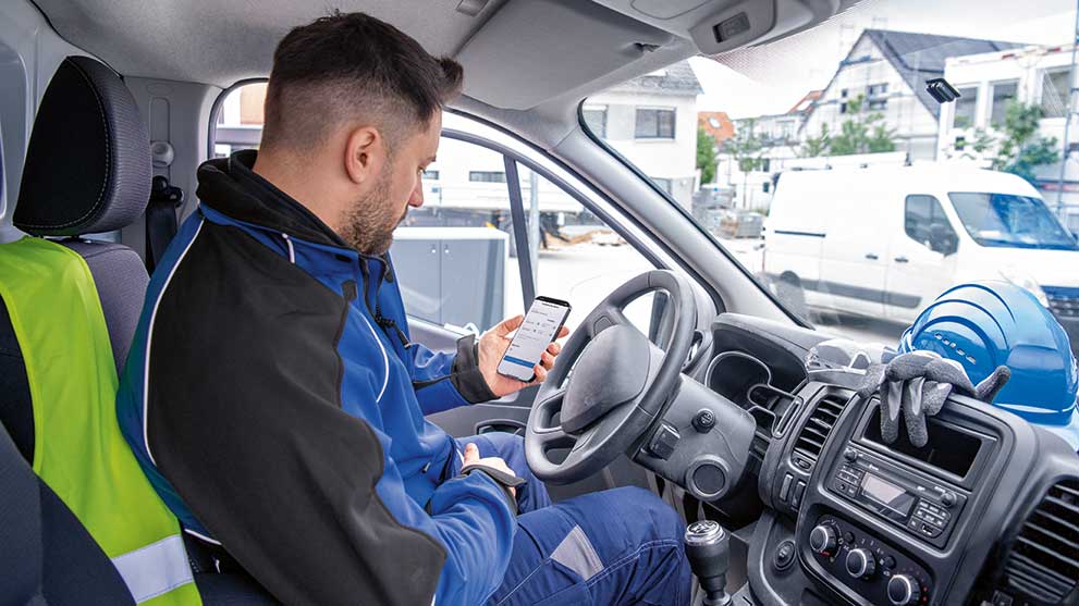Seorang pria dalam setelan kerja biru duduk di van dan melihat smartphone-nya.