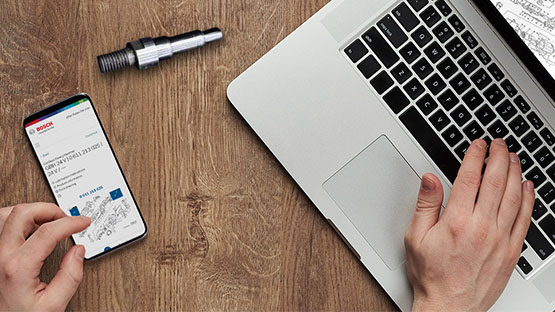 Sebuah smartphone dan laptop terletak di atas meja kayu, dengan alat di sampingnya.
